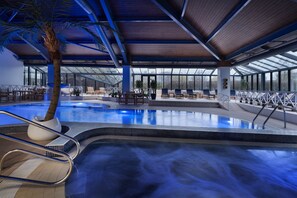 An indoor swimming pool with a wooden ceiling, seating areas, and a palm tree. - Delta Hotels by Marriott Peterborough (Peterborough)