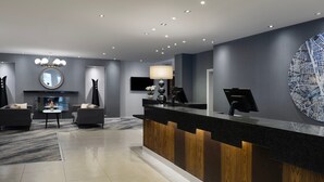 Un área de recepción moderna con un mostrador negro, paneles de madera, un espejo redondo, un televisor de pantalla plana, una chimenea y una gran obra de arte abstracta en la pared.
