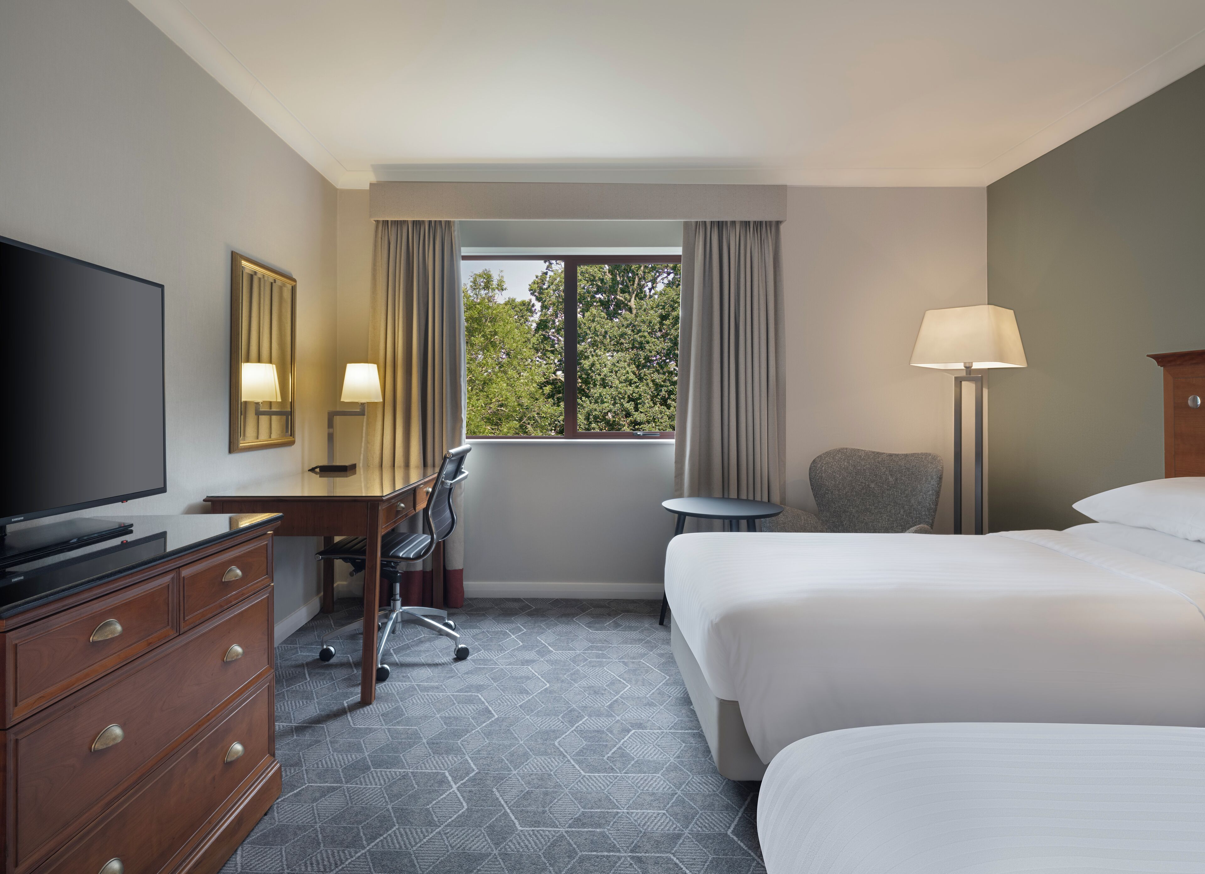 A hotel room with a bed, desk, chair, TV, and a window with curtains.