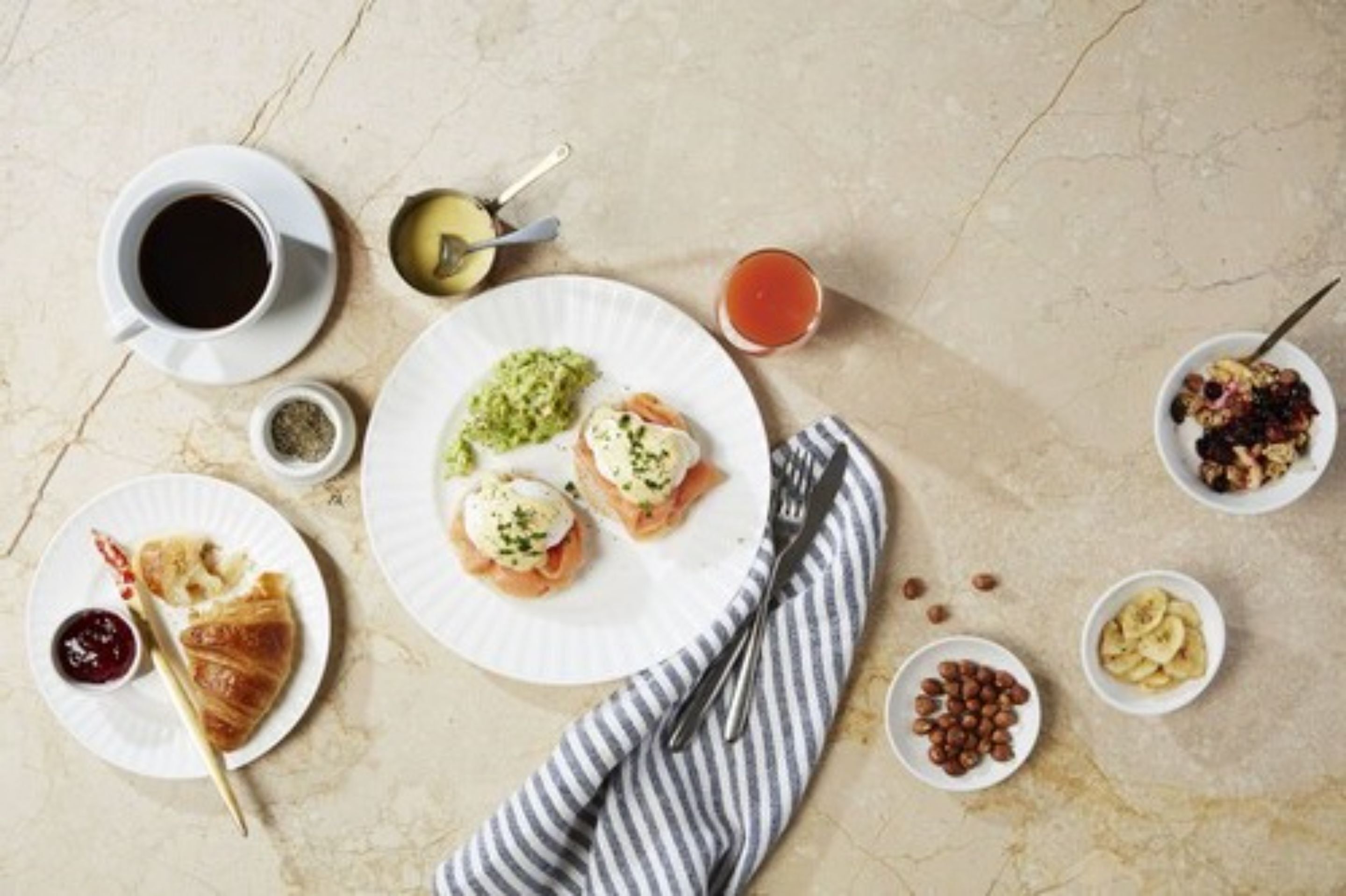 Un desayuno con croissant, huevos benedictinos, café, té y diferentes bocadillos.