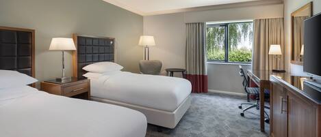 Quarto de hotel com duas camas, uma mesa, uma cadeira, uma televisão e uma janela com cortinas.