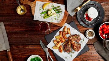 A wooden table with a variety of dishes including roasted potatoes, asparagus, and a steak with a side of peas.
