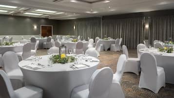 A conference room with multiple round tables, each set with white chairs, glassware, and floral centerpieces.