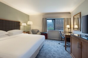 A hotel room with a large bed, two bedside lamps, a desk with a chair, a television, and a window with curtains. - Delta Hotels by Marriott Peterborough (Peterborough)