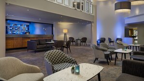 Un vestíbulo de hotel con una zona de bar, disposición de asientos y un techo alto con candelabros.