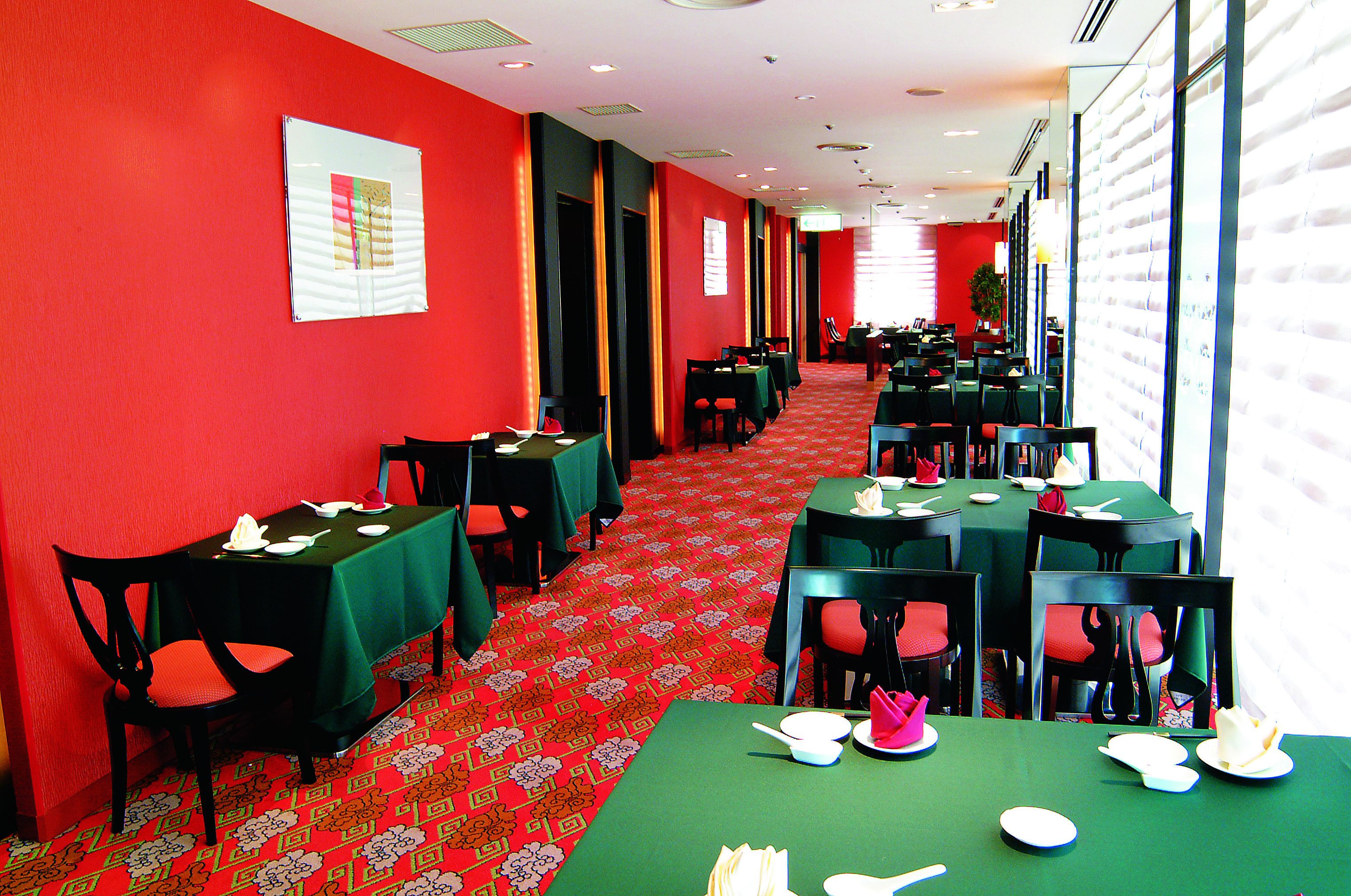 Uma sala de jantar de hotel com paredes vermelhas, mesas verdes e cadeiras pretas.
