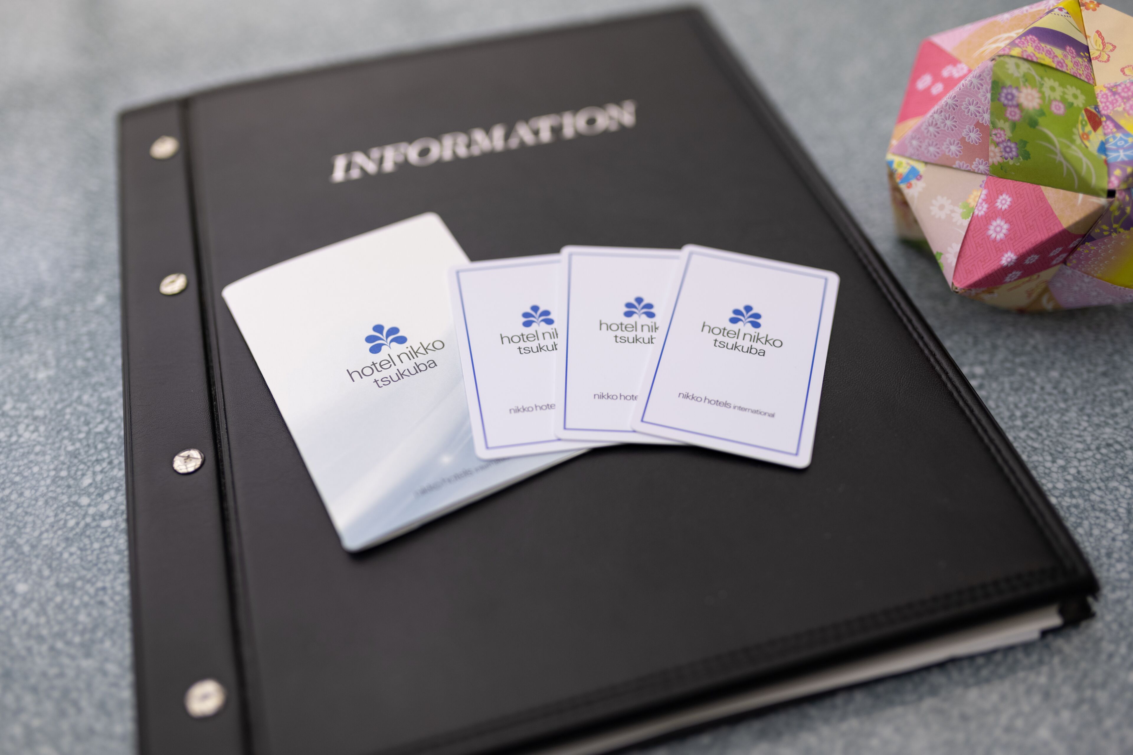 A black folder labeled "INFORMATION" with business cards and a colorful origami cube.