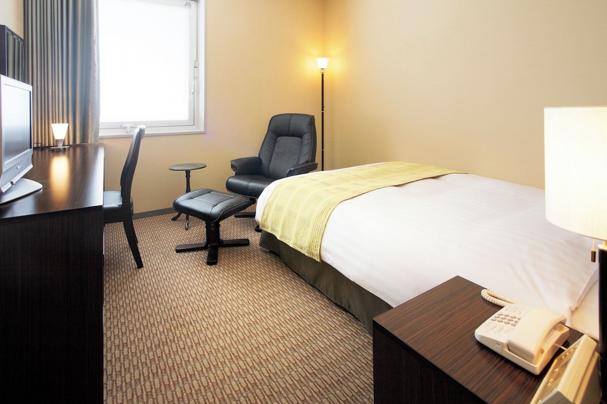 Habitación de hotel con cama, escritorio, computadora, silla, mesita y teléfono.