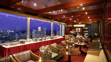 A high-rise hotel bar with a city view, red carpeted tables, and classic bar seating.
