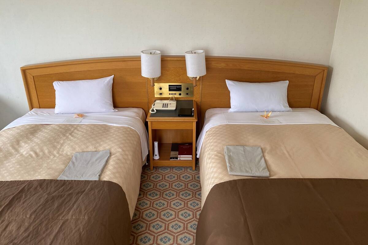 A hotel room with two beds, a wooden headboard, bedside lamps, a bedside table with a phone, and a patterned rug.