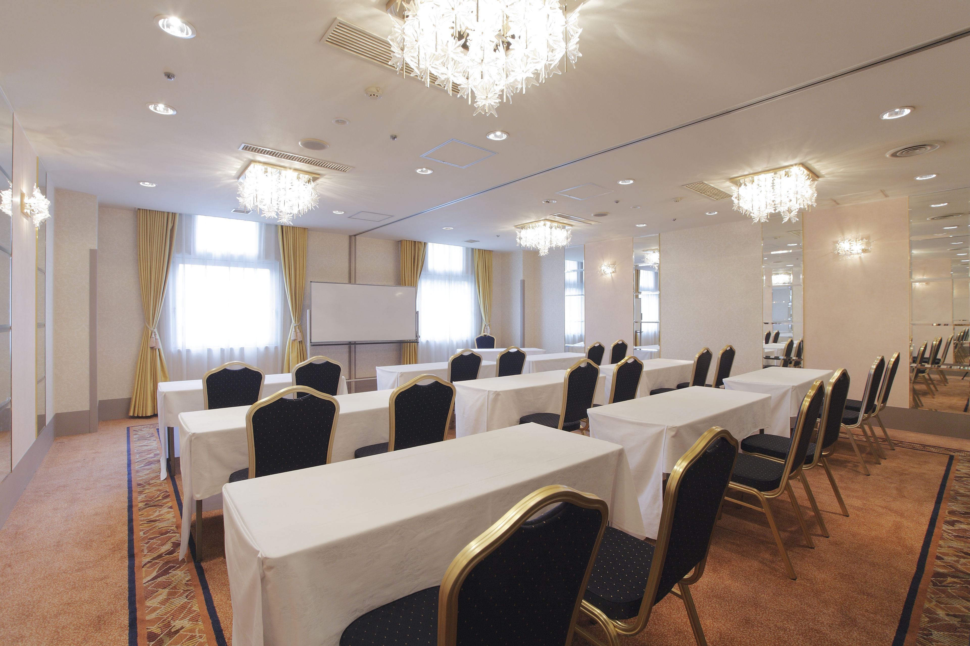 A conference room with tables and chairs, a projector screen, and a chandelier.
