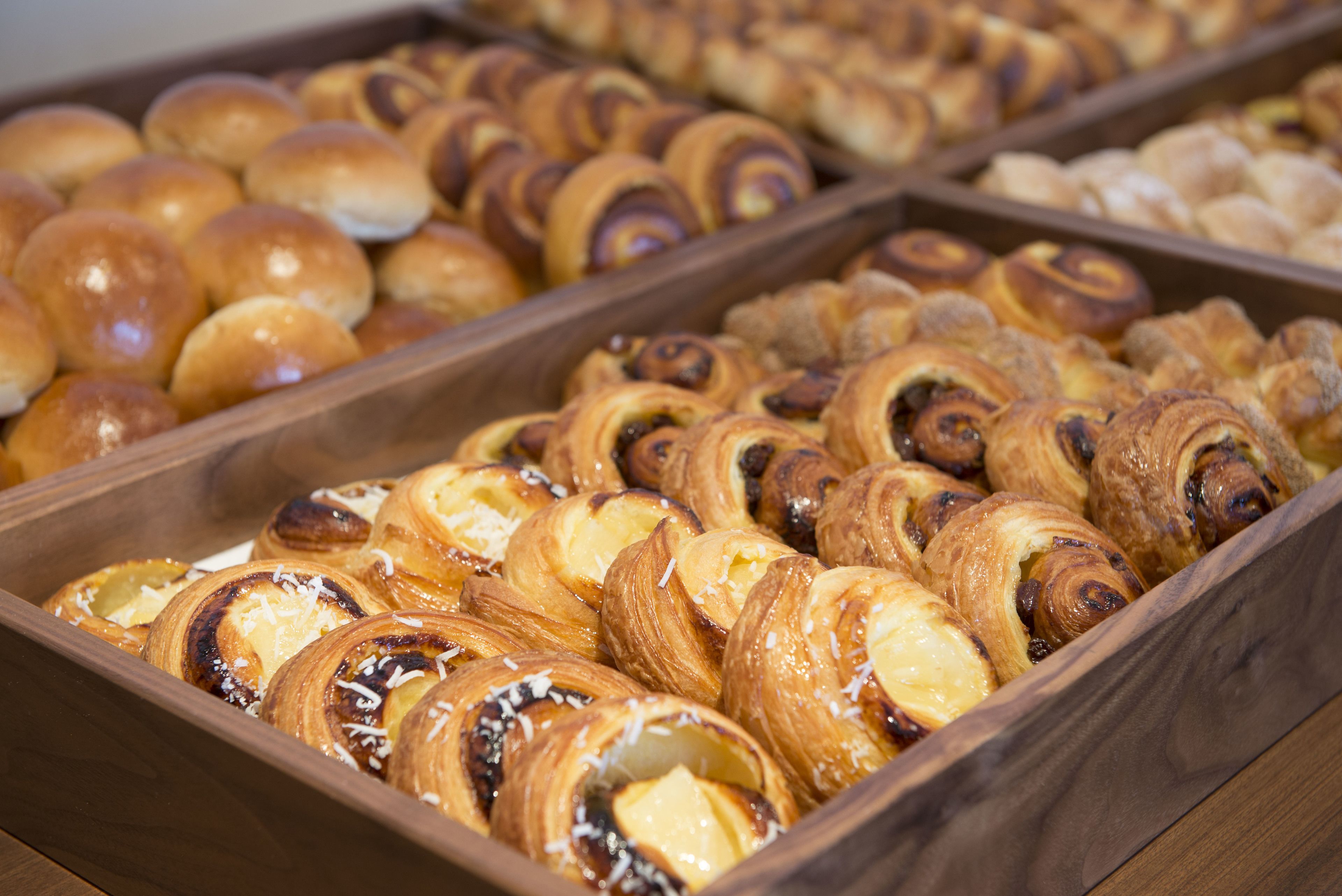 Uma bandeja de madeira com diversos doces, incluindo croissants e pães.