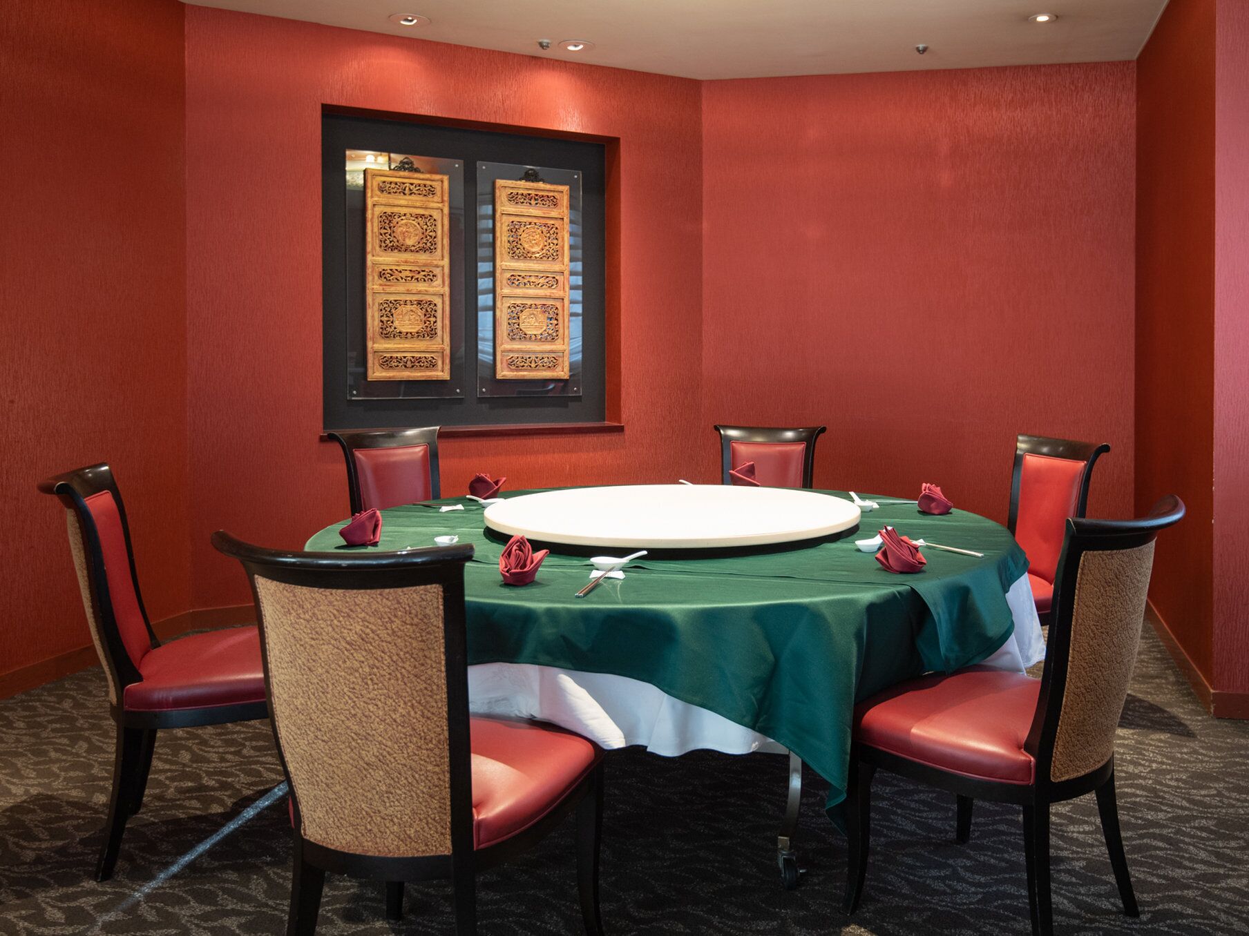 Un salón de conferencias con una mesa redonda, sillas rojas y un mantel verde.