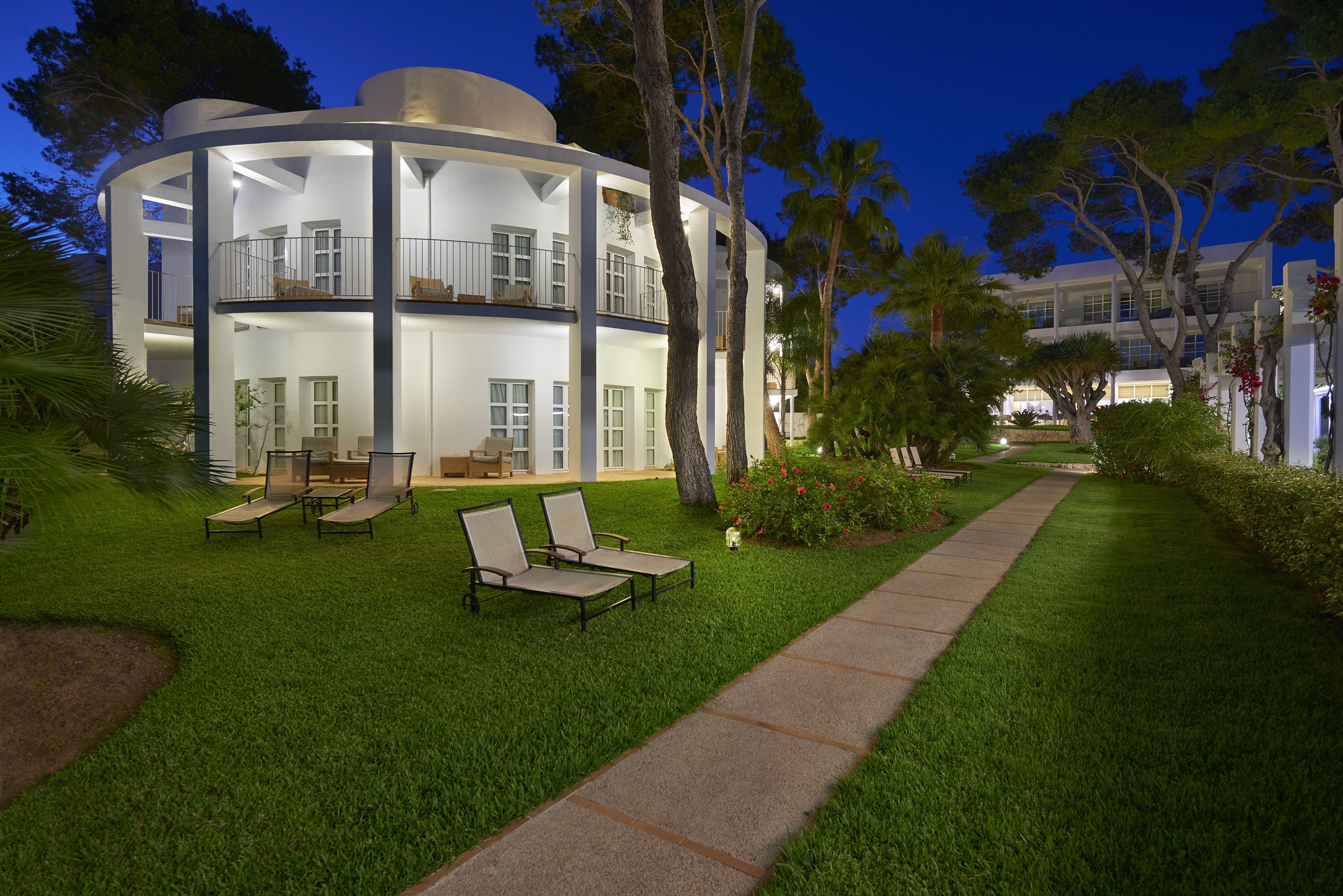 A modern, multi-story building with a circular design, featuring outdoor seating and a well-maintained lawn.