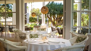 A restaurant with round tables set with white tablecloths, wicker chairs, and hanging wicker lamps.