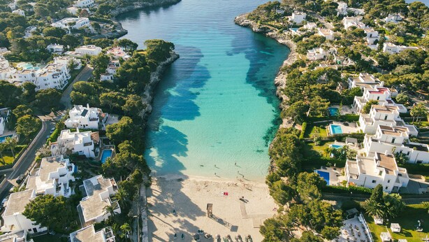 An aerial view of a coastal resort with white buildings, clear turquoise waters, and a sandy beach.