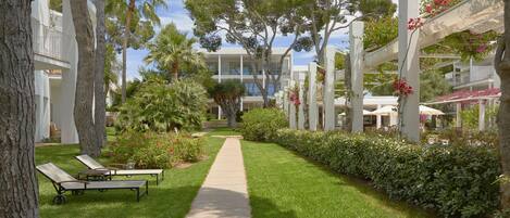 A pathway leading to a building with balconies, surrounded by trees and a well-maintained lawn.