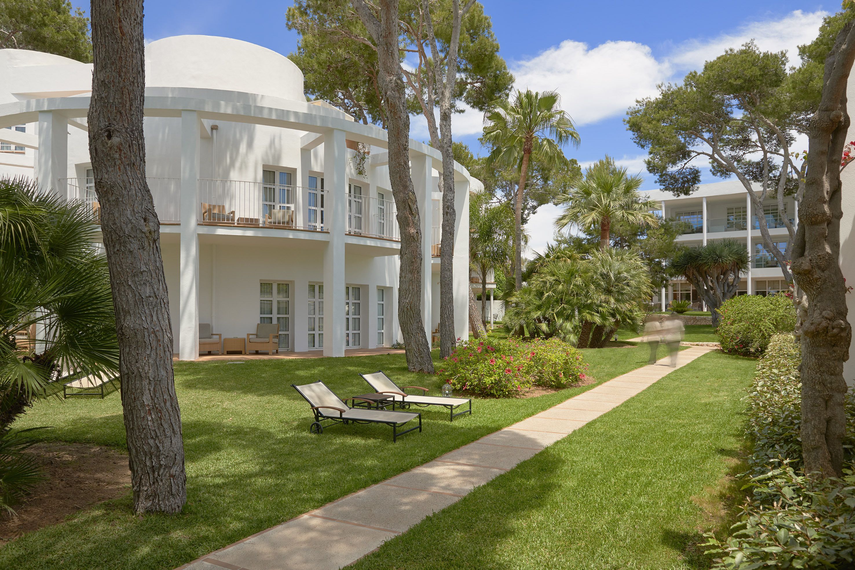 A modern building with a white exterior, a well-maintained lawn, and two lounge chairs.
