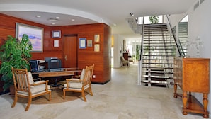 A spacious lobby with a wooden reception desk, two wooden chairs, a large potted plant, and a staircase with a glass railing. - Melia Cala d'Or Boutique Hotel (Santanyi)