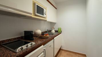 A compact kitchen with a built-in microwave, a kettle, and a coffee maker on the countertop.