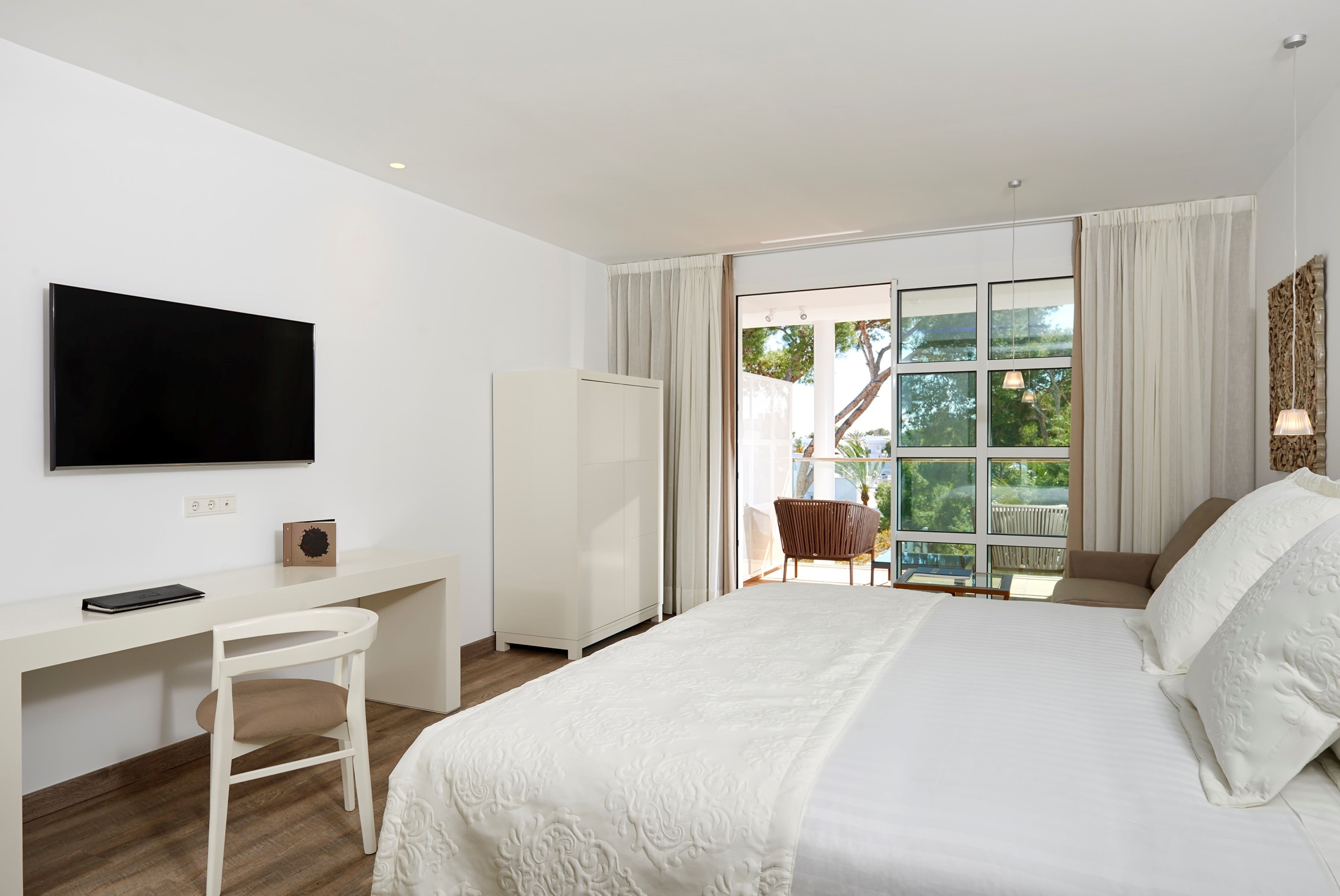 Une chambre d’hôtel moderne dotée d’un grand lit, d’un bureau avec une chaise, d’une télévision et d’une porte-fenêtre coulissante donnant sur un espace extérieur.