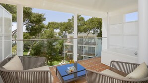 A balcony with wicker chairs, a glass table with drinks, and a view of a building and trees. - Melia Cala d'Or Boutique Hotel (Santanyi)