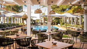 An outdoor pool area with lounge chairs, tables, and wicker lamps.