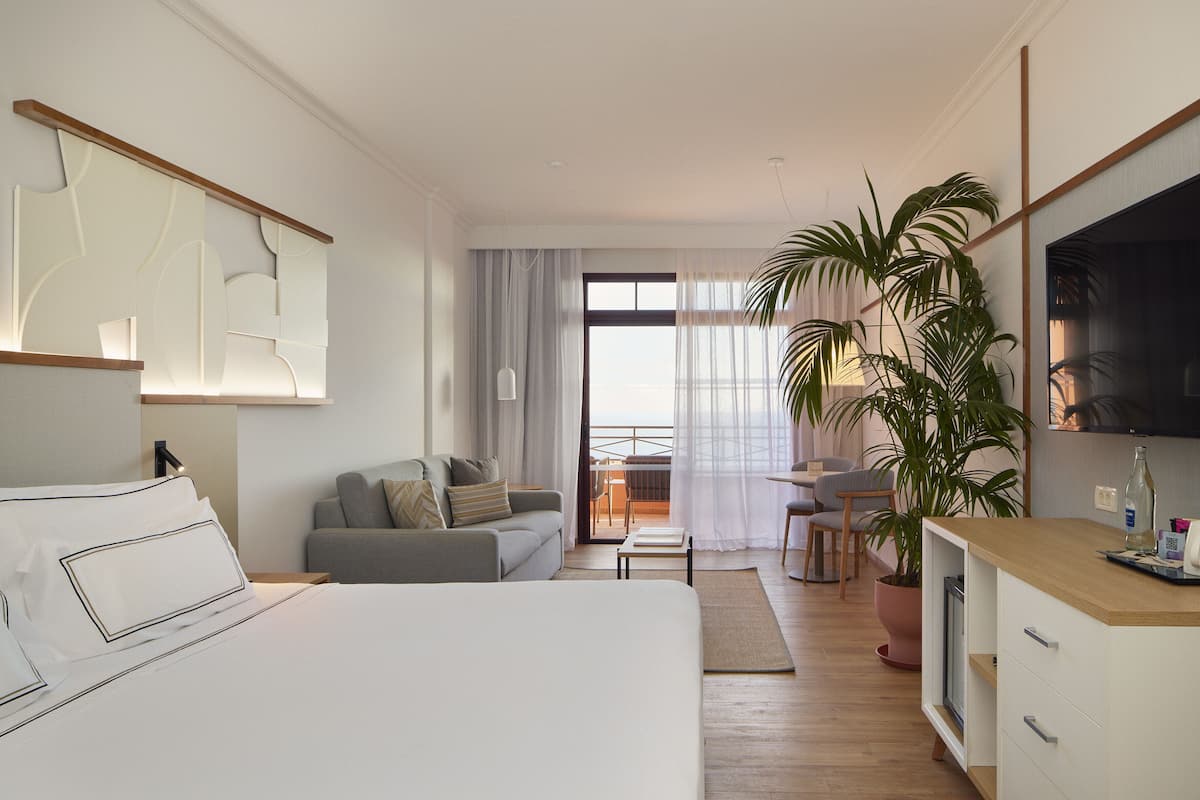 A modern hotel room with a large bed, a sofa, a dining area, and a TV.