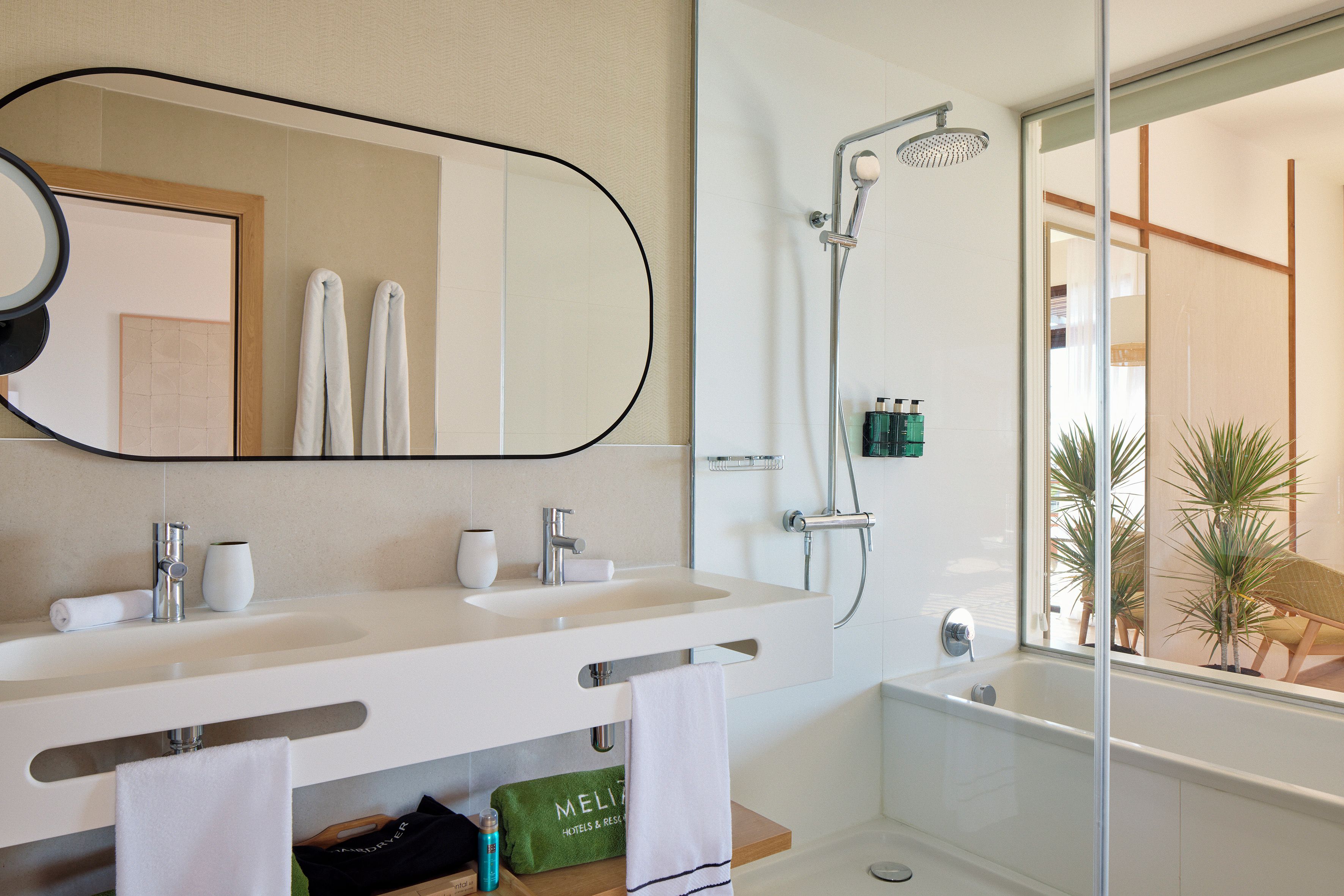 A modern bathroom with a large mirror, two sinks, a shower, and a bathtub.
