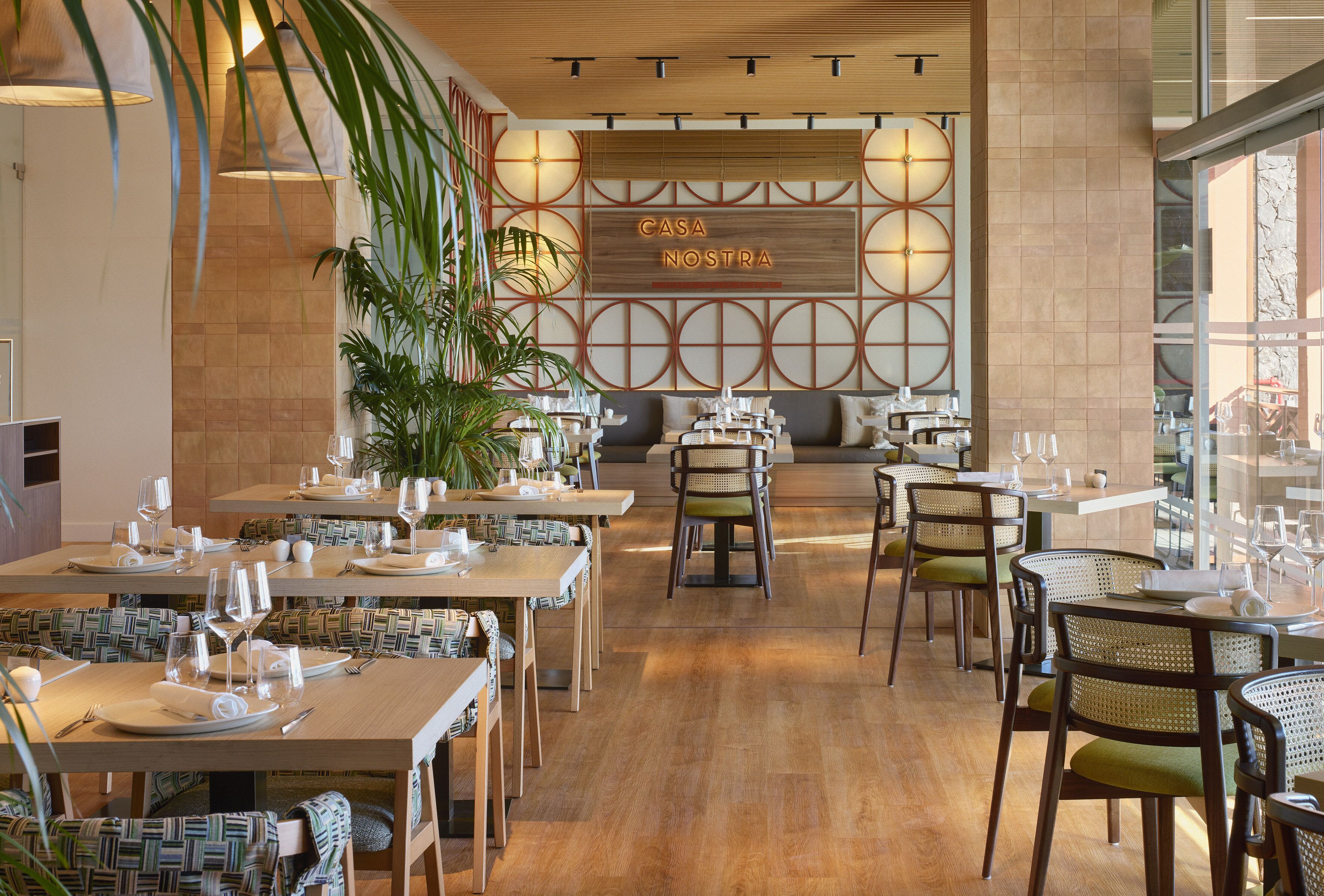 A restaurant with multiple dining tables and chairs, a wooden ceiling, and a wall with a circular pattern.