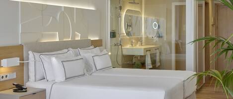 Una habitación de hotel moderna con una cama grande, mesita de noche y zona de ducha con paredes de vidrio.