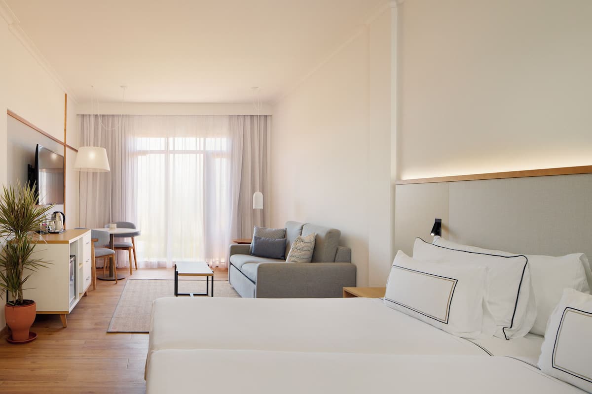 A hotel room with a large bed, a sofa, a desk, and a TV.