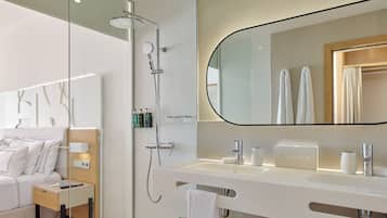 Un baño moderno con ducha, un espejo grande, un lavabo y una mesita de noche con lámpara.