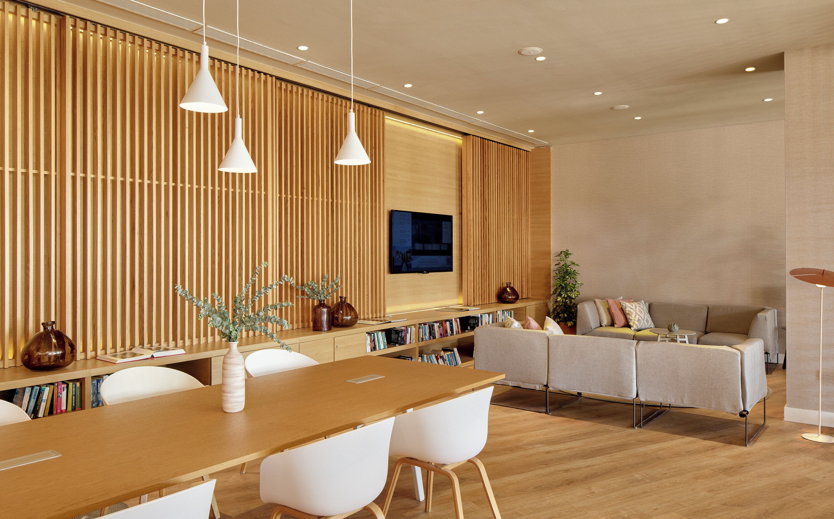 Una sala de estar moderna con una pared de acento de madera, un televisor de pantalla plana, un comedor con una mesa de madera y sillas blancas, y un sofá con cojines.