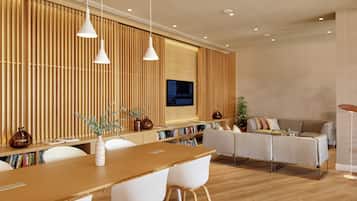 Una sala de estar moderna con una pared de acento de madera, un televisor de pantalla plana, un comedor con una mesa de madera y sillas blancas, y un sofá con cojines.