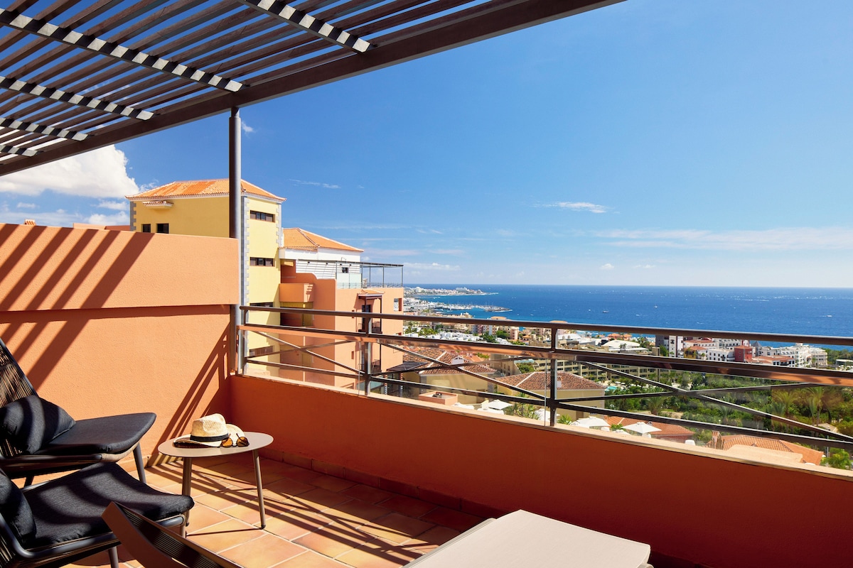 A balcony with a view of the sea, a table with a hat, and two chairs.