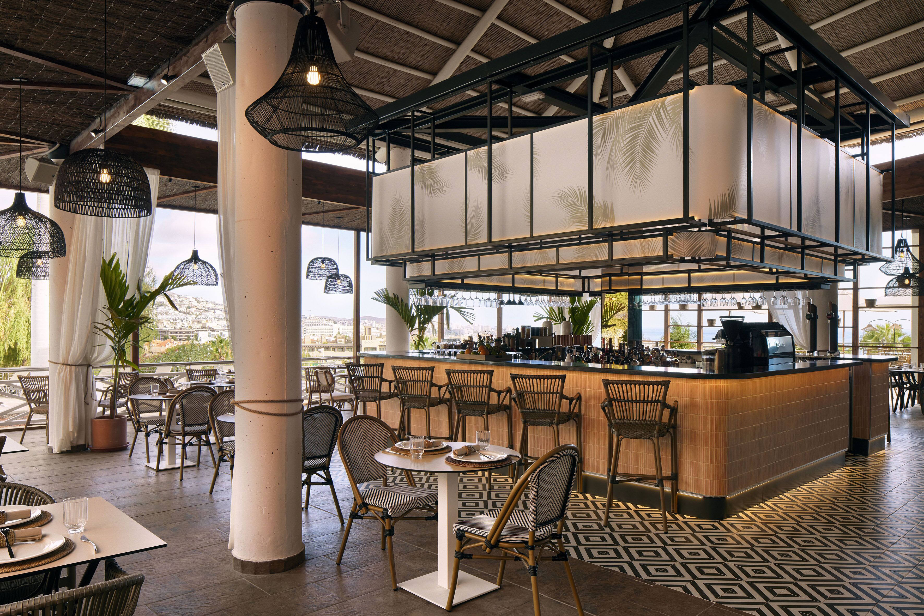 Un restaurante con zona de bar, sillas de mimbre y suelo estampado.