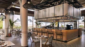 Un restaurante con zona de bar, sillas de mimbre y suelo estampado.