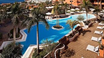 Un área de piscina en un resort con sillas de descanso, palmeras y una piscina azul cristalina.