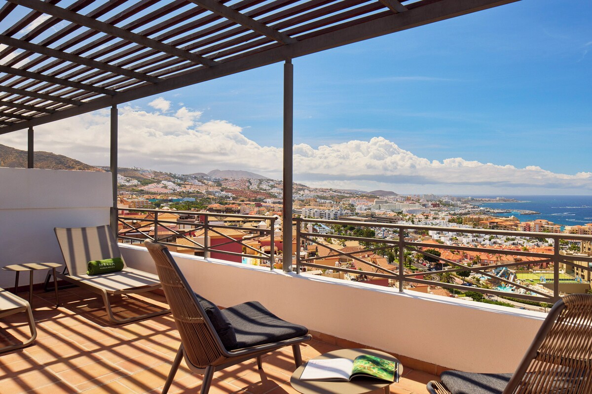 A balcony with a view of a coastal cityscape, a chair, and a table.