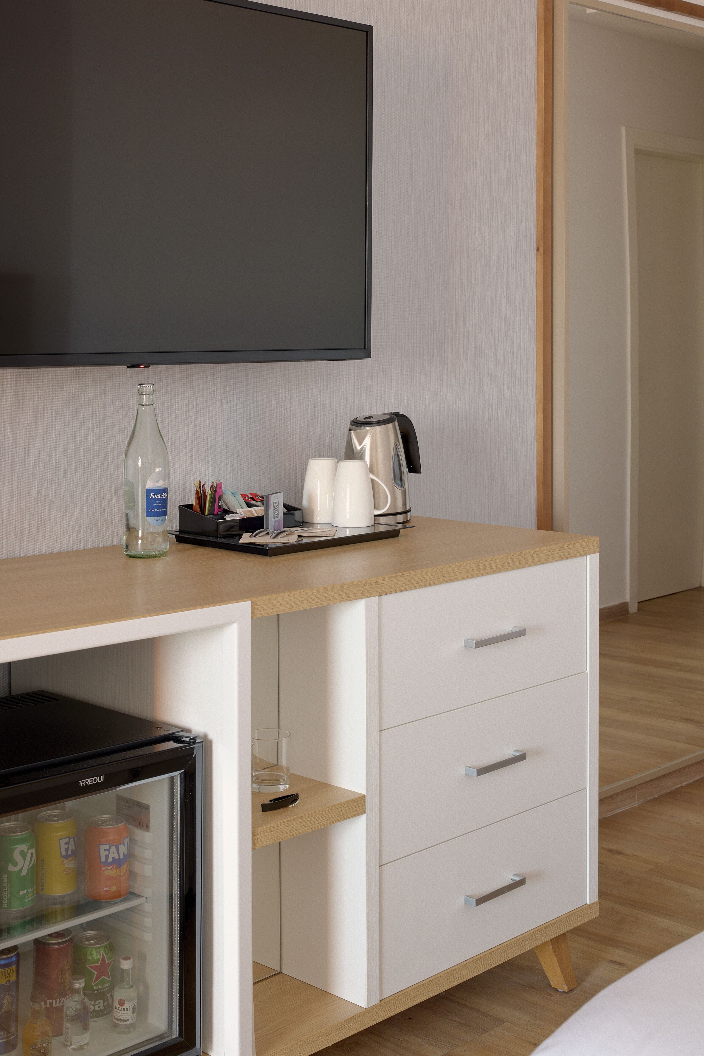 Une chambre d’hôtel équipée d’un bureau en bois, d’une télévision, d’un mini-réfrig érateur contenant des boissons et d’une machine à café.