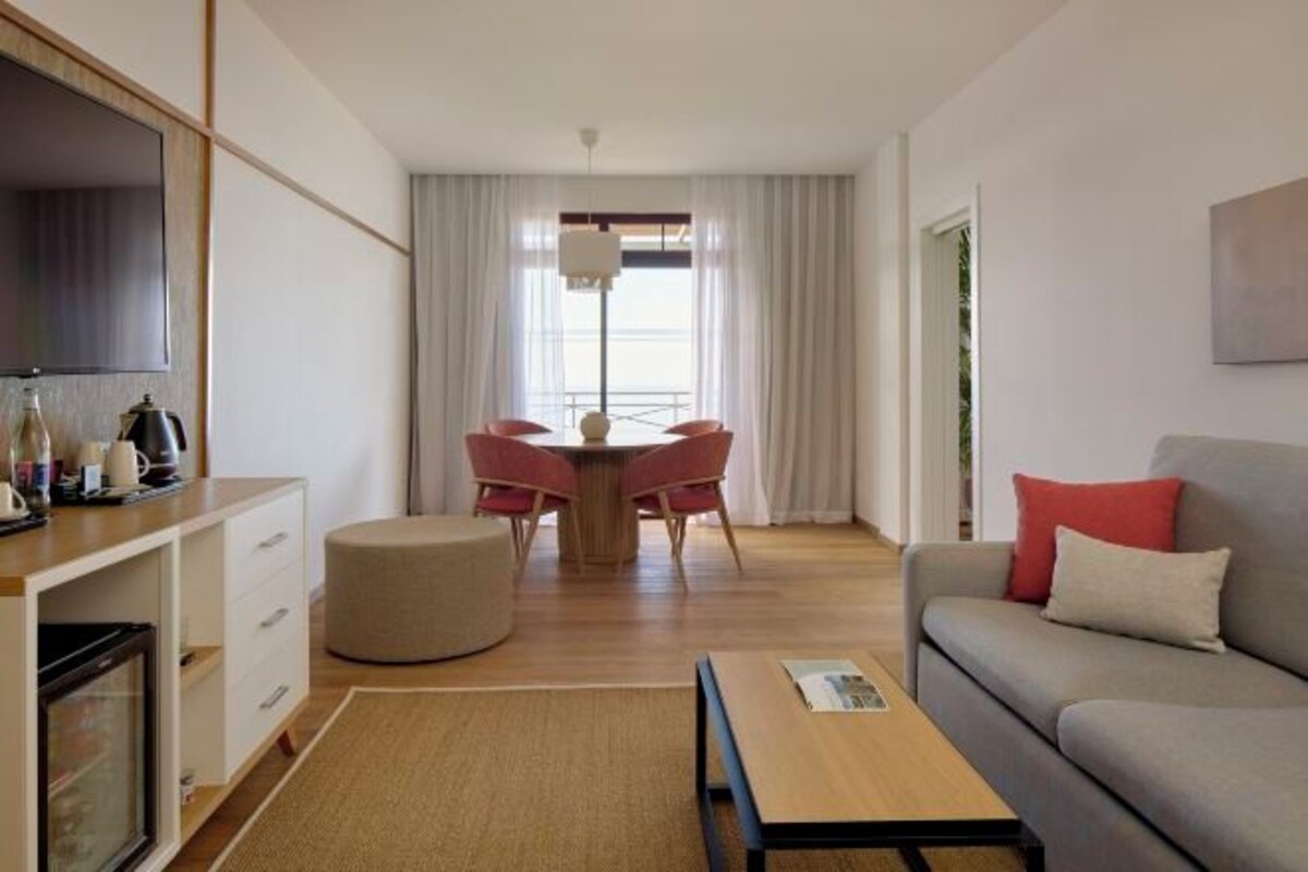 A modern living room with a flat-screen TV, a dining area with a table and chairs, a sofa with cushions, and a coffee table.