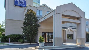 Entrada do hotel Sleep Inn com galeria coberta, uma grande árvore e céu claro.