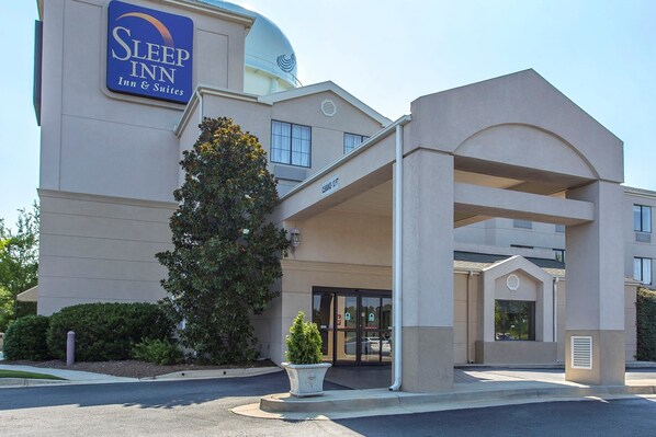 A Sleep Inn hotel entrance with a covered walkway, a large tree, and a clear sky.