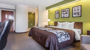 Quarto de hotel com cama, uma cadeira, uma escrivaninha e um abajur. Há quadros nas paredes.