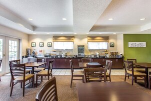 A spacious dining area with wooden tables and chairs, a kitchen in the background, and a green accent wall.