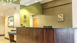 Uma mesa de recepção com acabamento em madeira, um letreiro da Sleep Inn & Suites e um certificado emoldurado na parede.