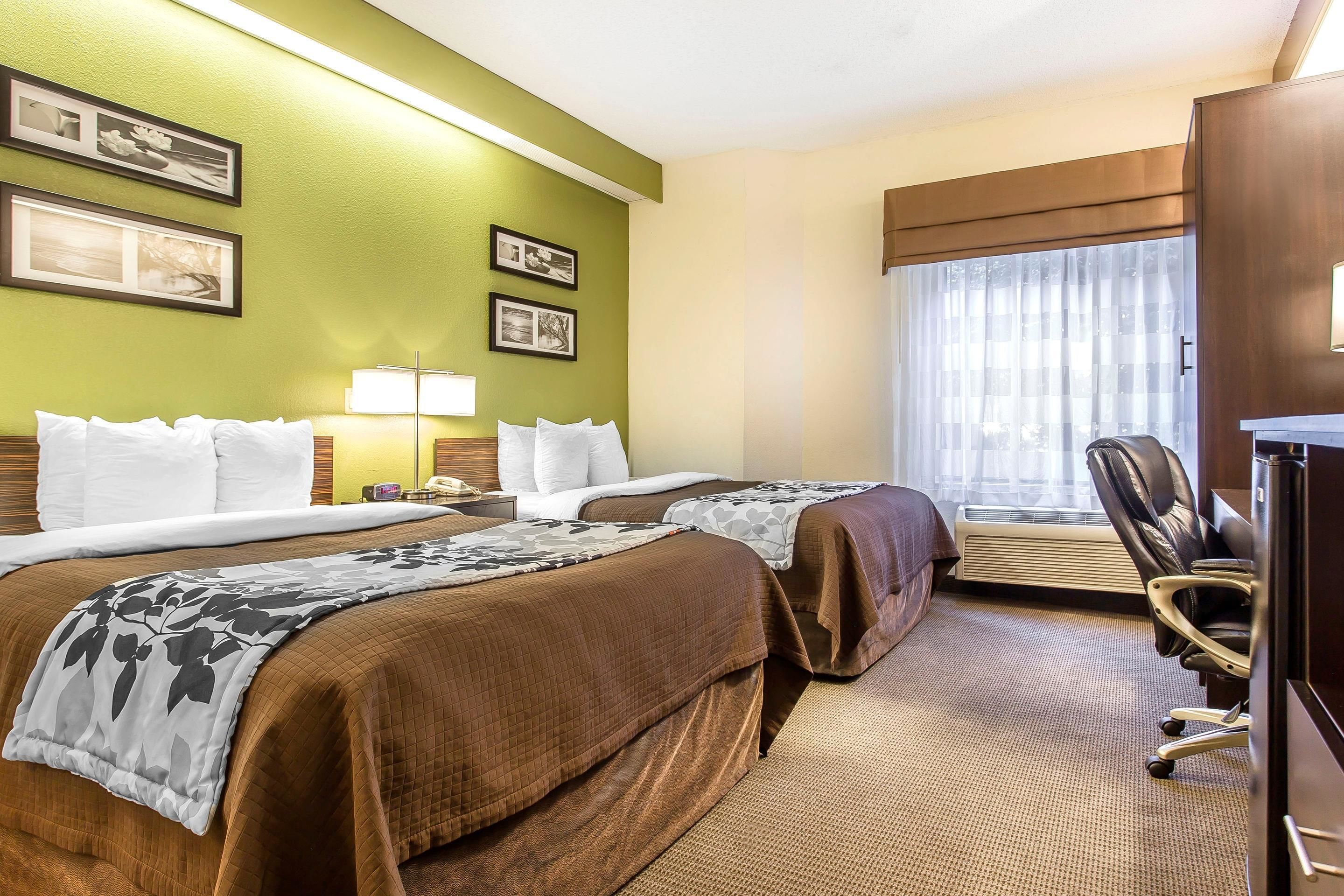 A hotel room with two beds, a desk, a chair, and a large window with curtains.