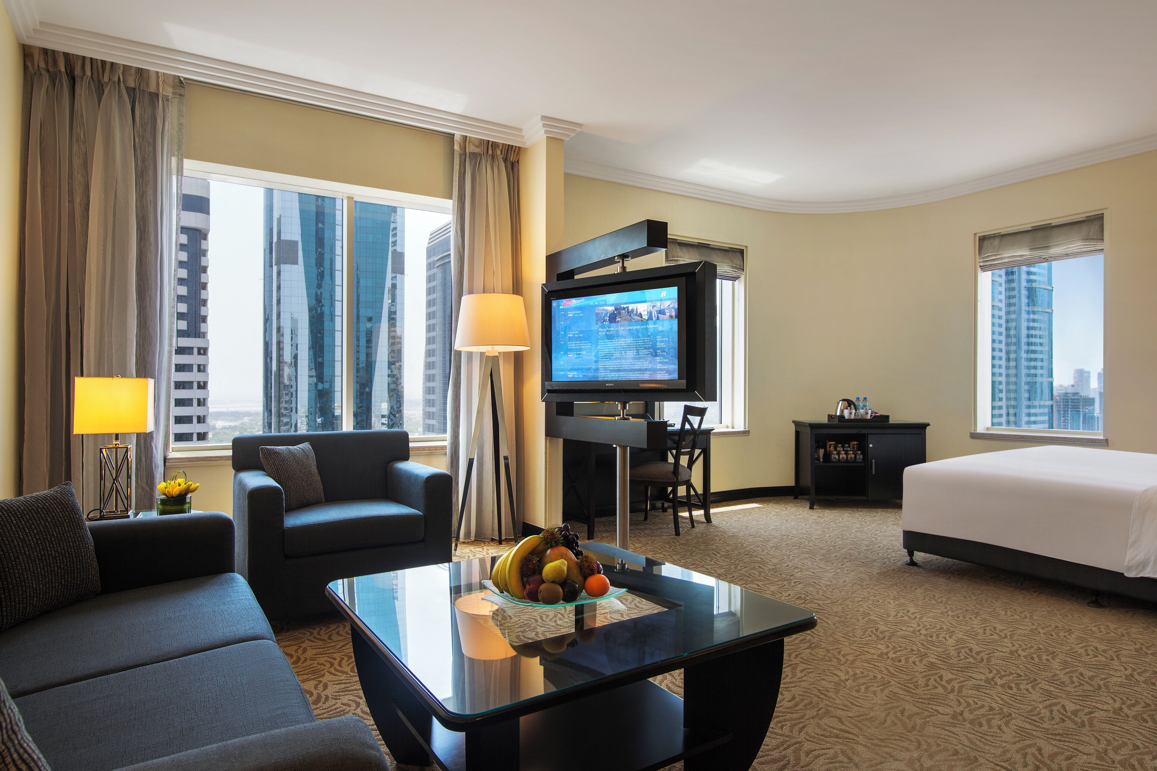 A hotel room with a bed, a sofa, a desk with a computer, a television, and a view of the city.
