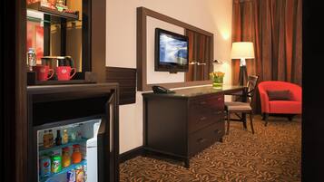 A hotel room with a minibar, a television, a desk with a chair, and a red sofa.